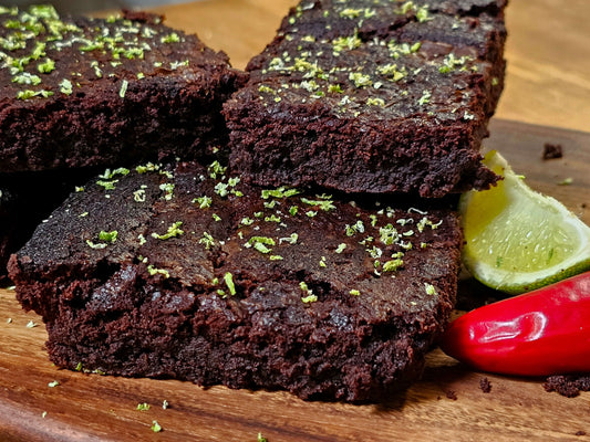 Close up of Dark chocolate and chili brownies. In front of them is a wedge of lime and chili. It is served on a wooden board